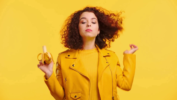 pleased curly girl eating ripe banana isolated on yellow - Footage, Video