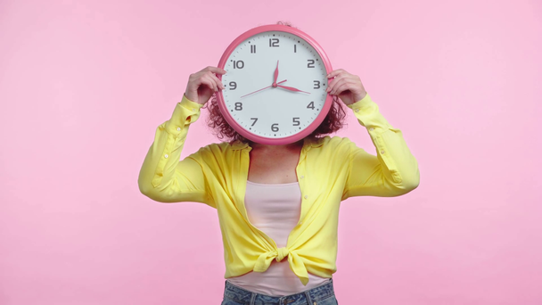 sorridente menina obscurecendo rosto com relógio redondo isolado em rosa
 - Filmagem, Vídeo