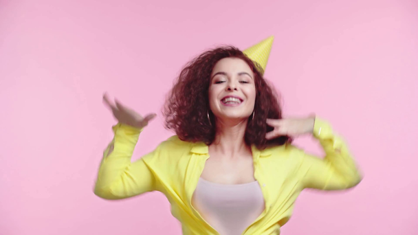 happy girl in party cap clapping hands and dancing isolated on pink - Felvétel, videó