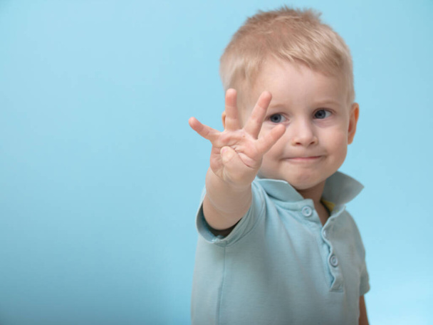 the baby shows on his fingers that he is four years old. concept of child development. baby on a blue background. space for your text - Photo, image