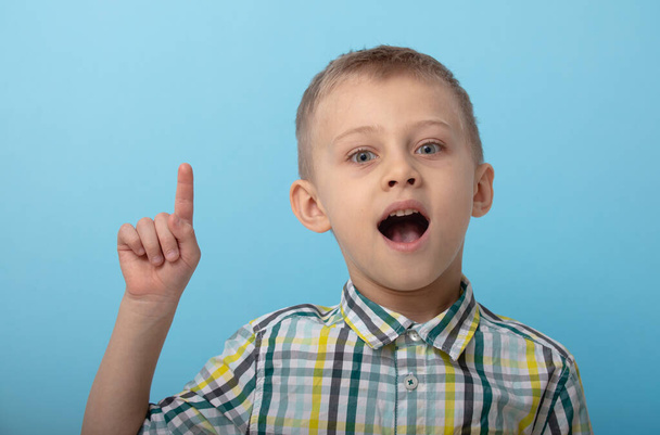 a boy in a plaid shirt poses on a blue background. the child shows emotions on the camera. concept of training and preparation for school - Foto, imagen