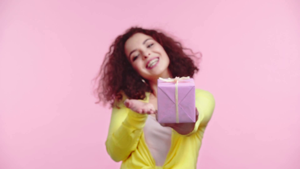 happy girl pointing with finger at gift box isolated on pink - Felvétel, videó