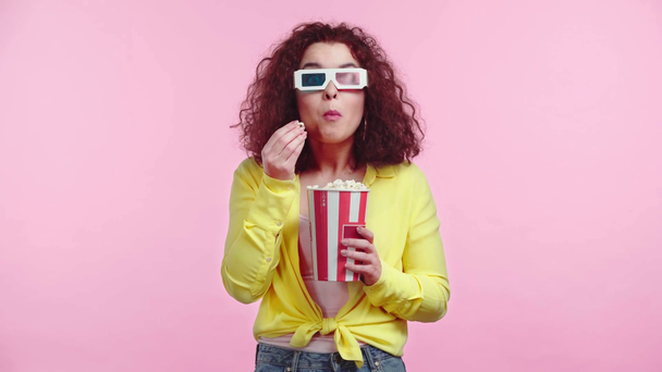 concentrated girl watching movie and eating popcorn isolated on pink - Filmagem, Vídeo