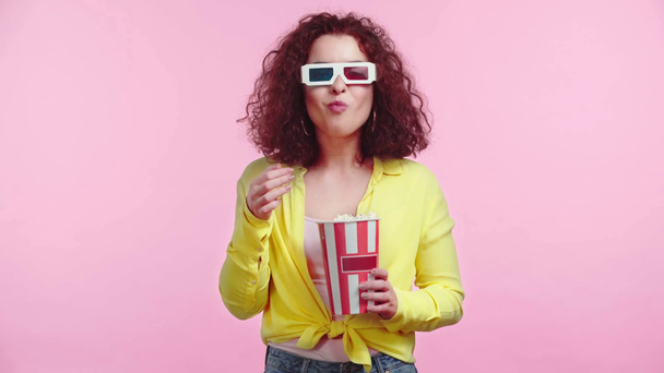 smiling girl eating popcorn while watching movie isolated on pink - Filmagem, Vídeo