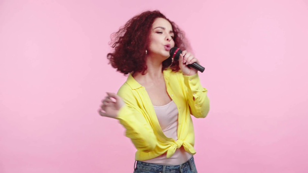 χαρούμενο κορίτσι που τραγουδάει με μικρόφωνο και χορεύει απομονωμένο στο ροζ - Πλάνα, βίντεο