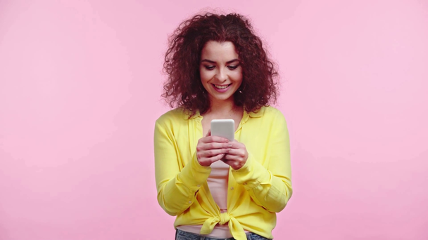 gelukkig meisje glimlachen terwijl chatten op smartphone geïsoleerd op roze - Video