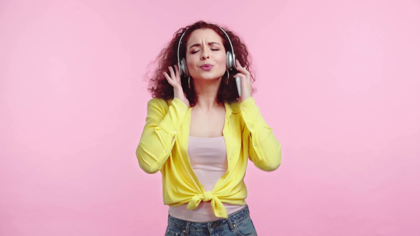 alegre chica bailando y cantando en auriculares inalámbricos aislados en rosa
 - Imágenes, Vídeo
