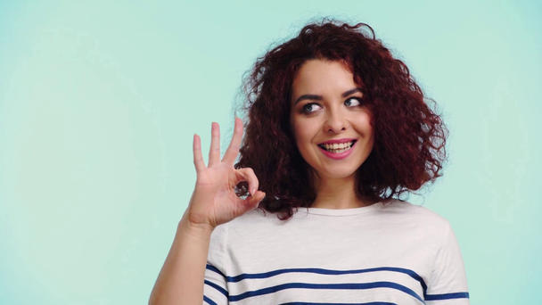 glücklich lockiges Mädchen zwinkert und zeigt okay Zeichen isoliert auf Türkis - Filmmaterial, Video