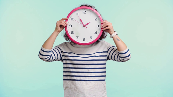 happy curly girl obscuring face with round clock isolated on turquoise - Footage, Video