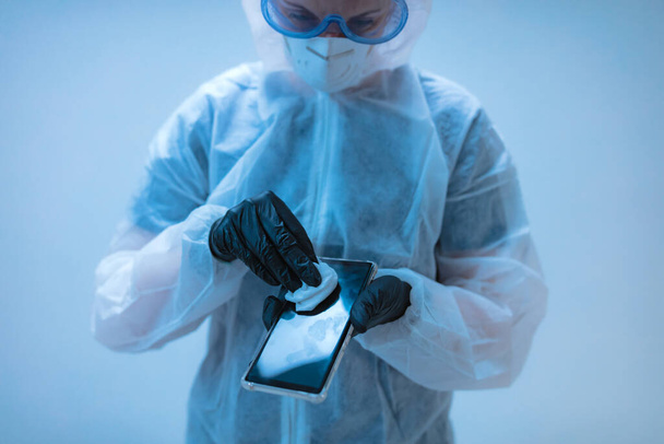 Medische arts, wetenschapper in pak voor de preventie van virussen en ziekten met een antiseptisch weefsel voor smartphone desinfectie. - Foto, afbeelding