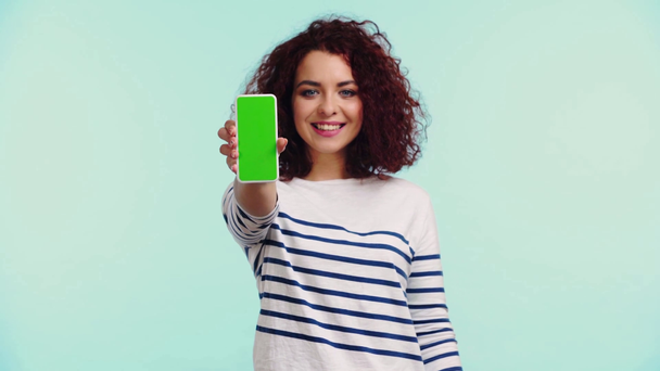 glückliches, lockiges Mädchen zeigt Smartphone mit grünem Bildschirm isoliert auf Türkis - Filmmaterial, Video