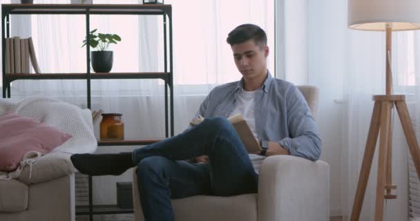 Millennial guy reading popular book at home - Materiaali, video