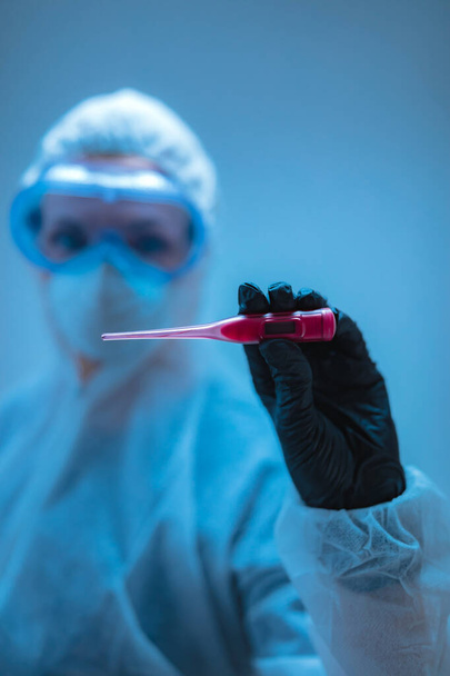 Arzt, Wissenschaftler im Ganzkörperanzug zur Vorbeugung gegen Viren und Krankheiten mit einem Thermometer für die Körpertemperatur. - Foto, Bild
