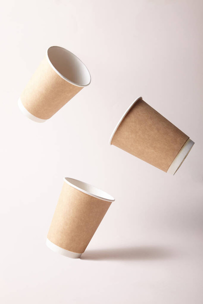 tres vasos vacíos de papel vuelan sobre fondo de papel marrón
 - Foto, imagen