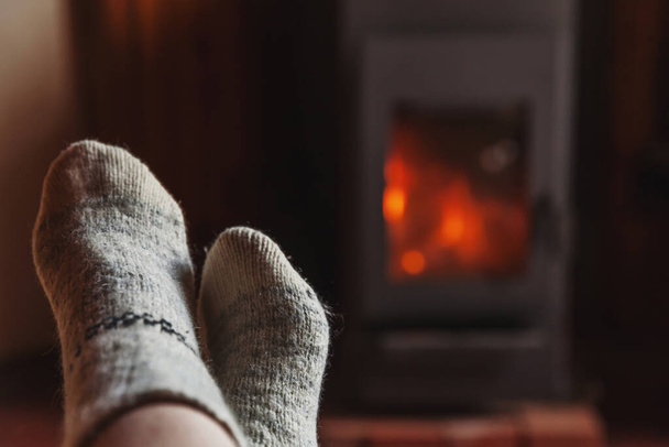 Kış kıyafetlerinin içinde ayaklar şömine arkasında yün çoraplar. Kadın kış ya da sonbahar akşamları evde oturup dinleniyor ve ısınıyor. Kış ve soğuk hava kavramı. Hygge Noel arifesi - Fotoğraf, Görsel