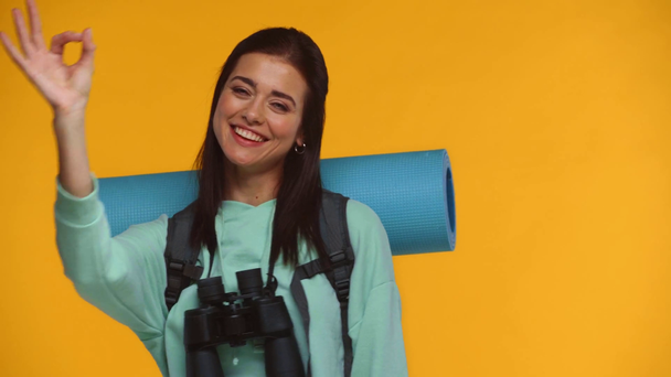 Glimlachende toerist toont ok gebaar op camera geïsoleerd op geel - Video