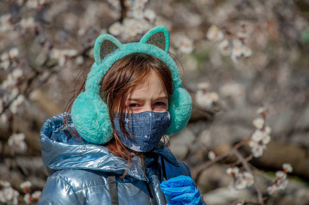 屋外の保護マスクの女性。屋外でマスクの女の子。ウィルスマスク春。9歳の少女。通りだ。ウイルスや細菌からの保護。医療用呼吸マスク。伝染病だ。保護 - 写真・画像