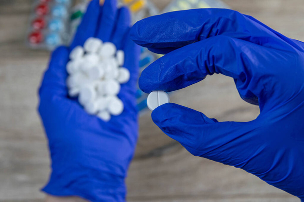 Many small white pills in the hands of a doctor wearing medical blue disposable gloves. Hands take one pills. - Photo, image
