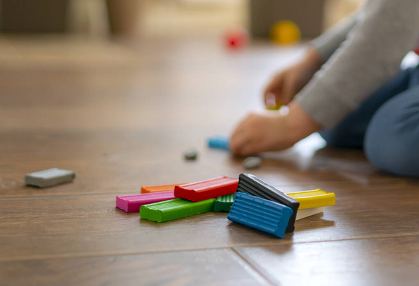 A gyermek játszik színes műanyag modellezés a fa padlón - Fotó, kép