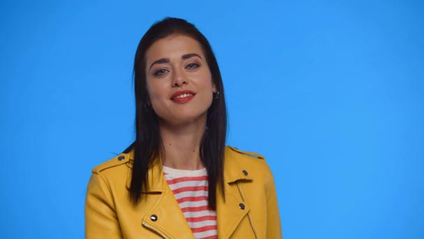 Menina atraente na jaqueta amarela sorrindo para a câmera isolada no azul
 - Filmagem, Vídeo