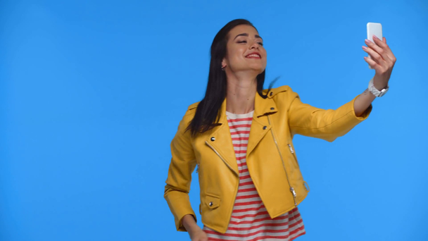 Hymyilevä tyttö keltainen takki ottaen selfie älypuhelimella eristetty sininen
 - Materiaali, video