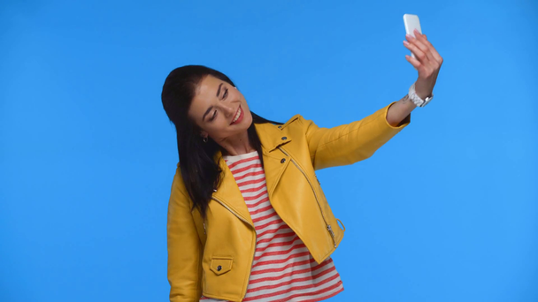 Hermosa mujer tomando selfie con teléfono inteligente aislado en azul
 - Metraje, vídeo
