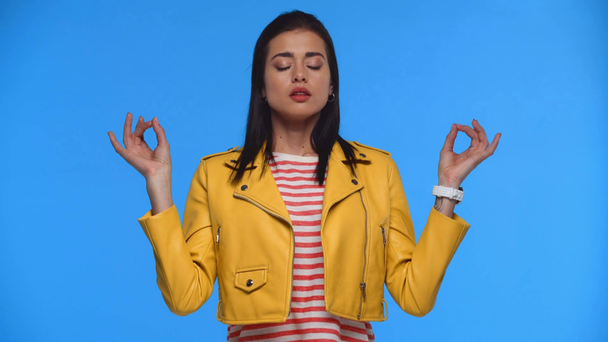 Schöne Mädchen in gelber Jacke meditieren isoliert auf blau - Filmmaterial, Video