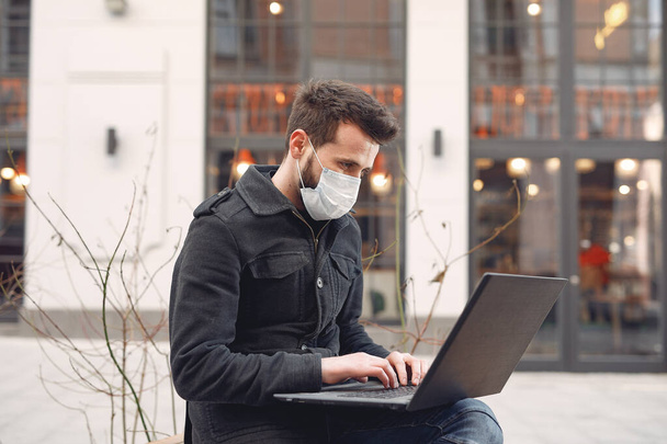 Man in a mask sitting in the city with a laptop - Foto, Imagen
