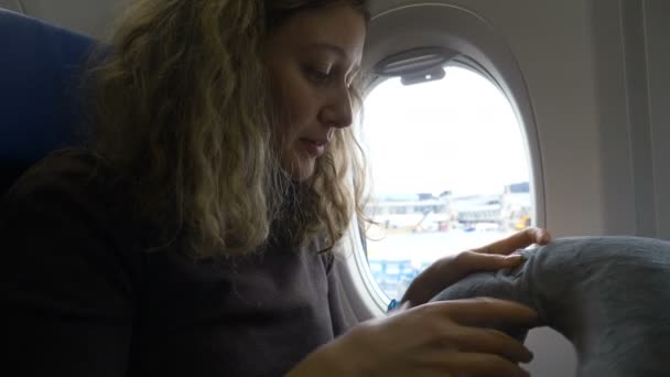 girl puts pillow under neck for trip before takeoff - Felvétel, videó