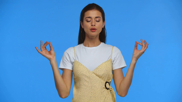 Beautiful girl meditating and looking at camera isolated on blue - Footage, Video