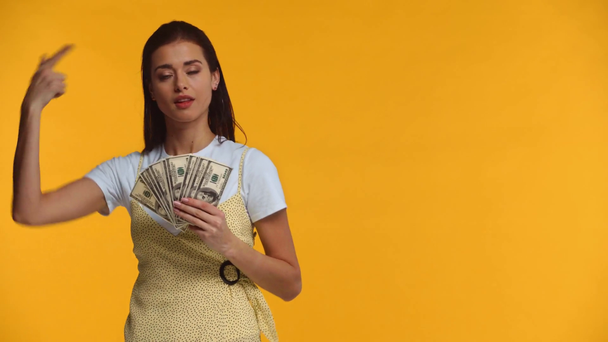 Beautiful girl pointing with finger on dollar banknotes isolated on yellow - Video, Çekim