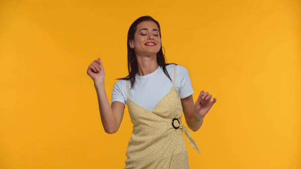 Chica positiva bailando y sonriendo a la cámara aislada en amarillo
 - Metraje, vídeo