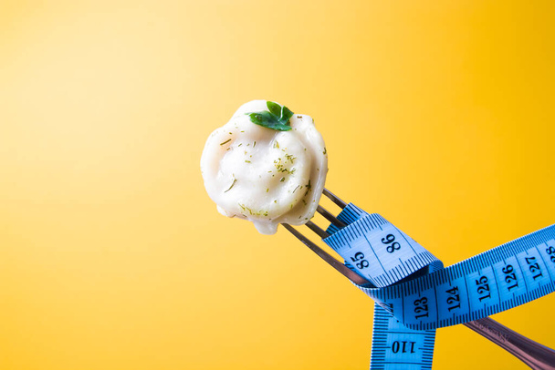 one dumpling with a leaf of parsley on a fork, a measured blue tape wrapped around the fork to measure waist and body volume, weight loss and diet concept - Photo, Image