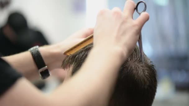 Fiatal férfiak hajvágása a fodrászatban. Közelkép a mester nyírás haj ollóval és fésűvel - Felvétel, videó
