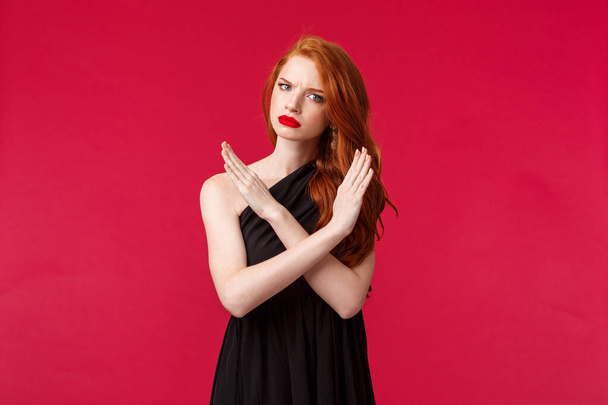 Fashion, luxury and beauty concept. Portrait of serious and displeased, mad young sassy redhead girl in black dress, making cross stop sign, grimacing with disapproval, disagree and reject - Photo, Image