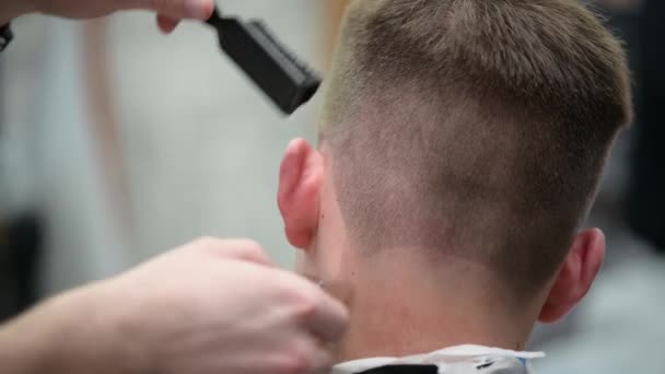 Młody fryzjer w Barbershop. Zbliżenie mistrza strzyżenia włosów z przycinaczem - Materiał filmowy, wideo