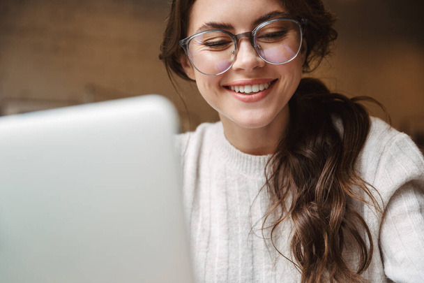 Image of young beautiful caucasian woman wearing eyeglasses using silver laptop in cafe - Φωτογραφία, εικόνα