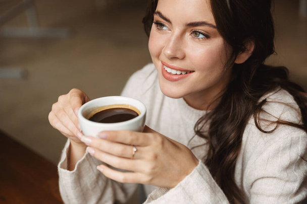 Image of young beautiful caucasian woman with long brown hair smiling while drinking coffee in cafe - Zdjęcie, obraz