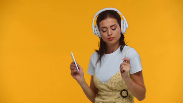 meisje in hoofdtelefoon dansen en houden smartphone geïsoleerd op geel - Video