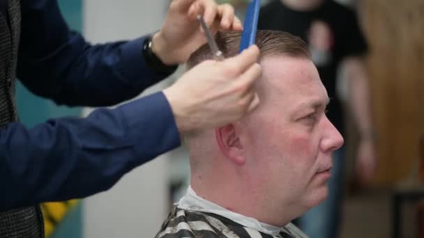 Чоловіча стрижка в перукарні. Крупним планом майстер відсікає чоловіка з світлим волоссям з застібкою
 - Кадри, відео
