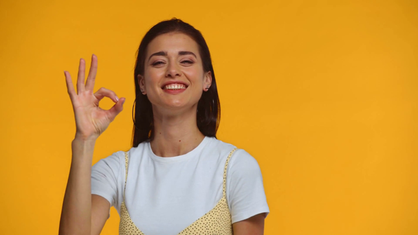 glimlachende vrouw tonen oke gebaar op camera geïsoleerd op geel - Video