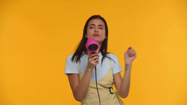 Happy girl śpiew i taniec z suszarką do włosów izolowane na żółty - Materiał filmowy, wideo