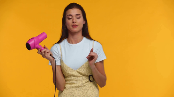 Aantrekkelijke vrouw met roze föhn geïsoleerd op geel - Video