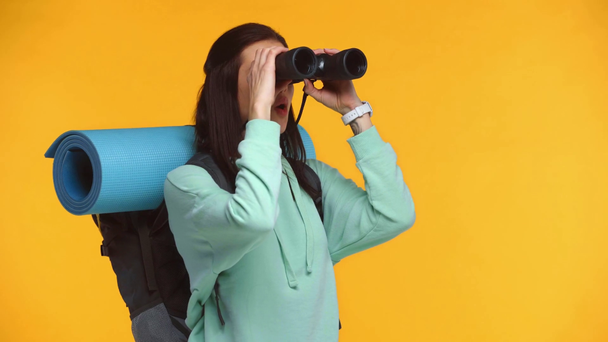 Aufgeregter Reisender mit Rucksack blickt auf Fernglas isoliert auf gelb - Filmmaterial, Video