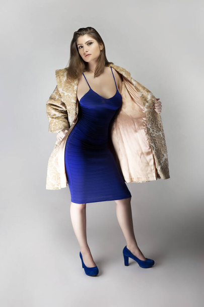 Female fashion model wearing a beige brocade wool or cotton coat and a blue sexy dress in studio catalog style.  Depicts spring or fall trends - Фото, зображення