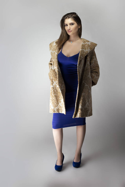 Female fashion model wearing a beige brocade wool or cotton coat and a blue sexy dress in studio catalog style.  Depicts spring or fall trends - Foto, imagen
