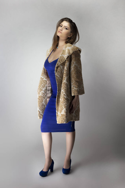 Female fashion model wearing a beige brocade wool or cotton coat and a blue sexy dress in studio catalog style.  Depicts spring or fall trends - Valokuva, kuva