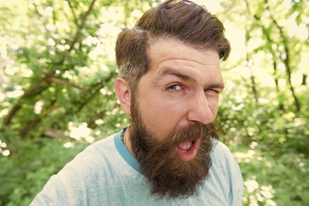 The mustache made me do it. Bearded man winking with stylish mustache shape. Brutal hipster with textured mustache hair on unshaven face. Caucasian guy wearing long beard and mustache outdoor - Foto, Bild