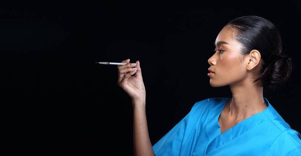 Asian Beautiful Doctor Pielęgniarka tan skóry kobieta w niebieskim mundurze ze strzykawką, portret pół ciała tworzą czarne włosy, studio oświetlenie ciemne tło kopia przestrzeń prezentacji obszar - Zdjęcie, obraz