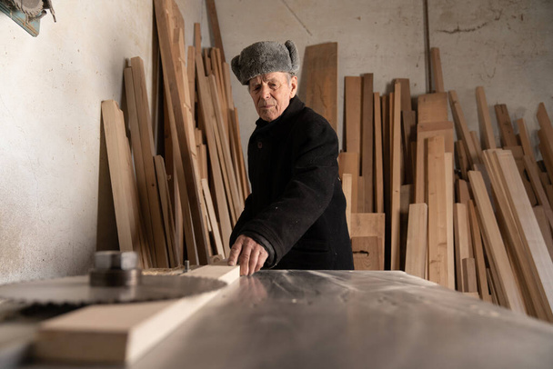 Европейский плотник, работающий на деревянном рабочем столе в столярном цехе. Старый европеец работает в столярном магазине.
. - Фото, изображение